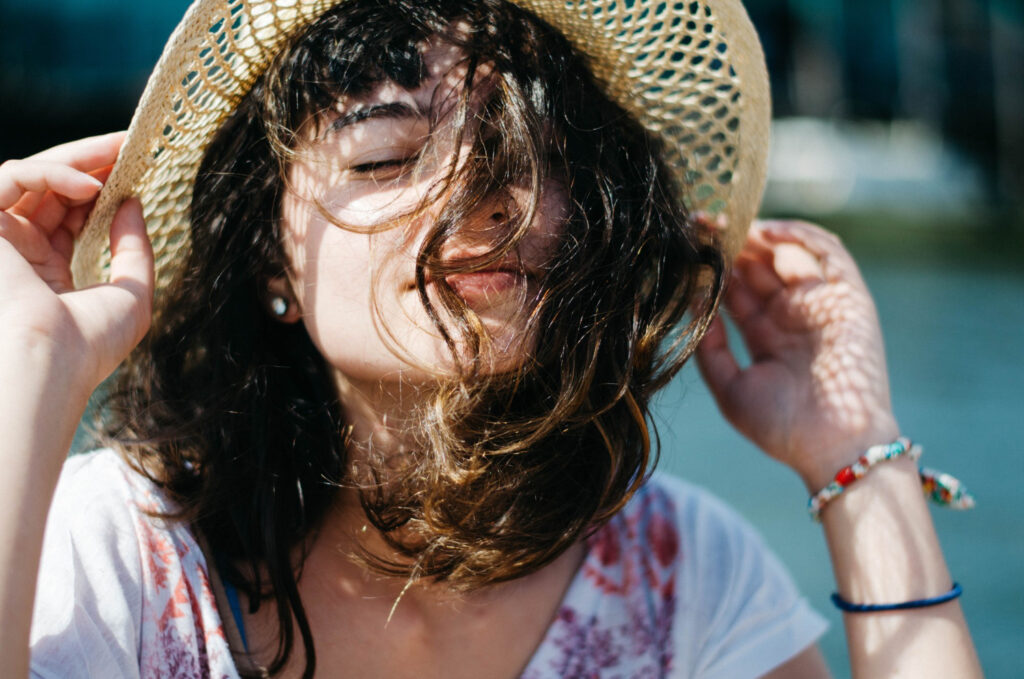 mulher na praia com chapeu se protegendo do sol